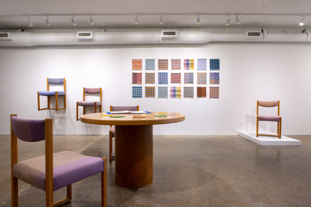 Exhibition image featuring a large room with didactic poster, chairs, and textile samples. 